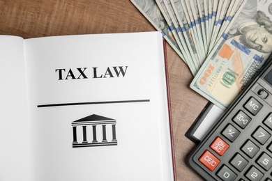 Photo of Calculator, money and book with words TAX LAW on table, top view