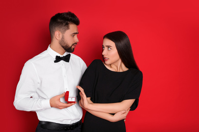 Photo of Young woman rejecting engagement ring from boyfriend on red background
