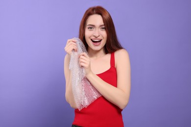 Woman popping bubble wrap on purple background. Stress relief
