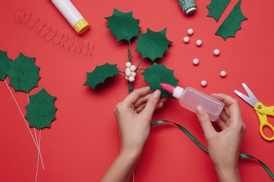 Woman making mistletoe branch on red background, top view