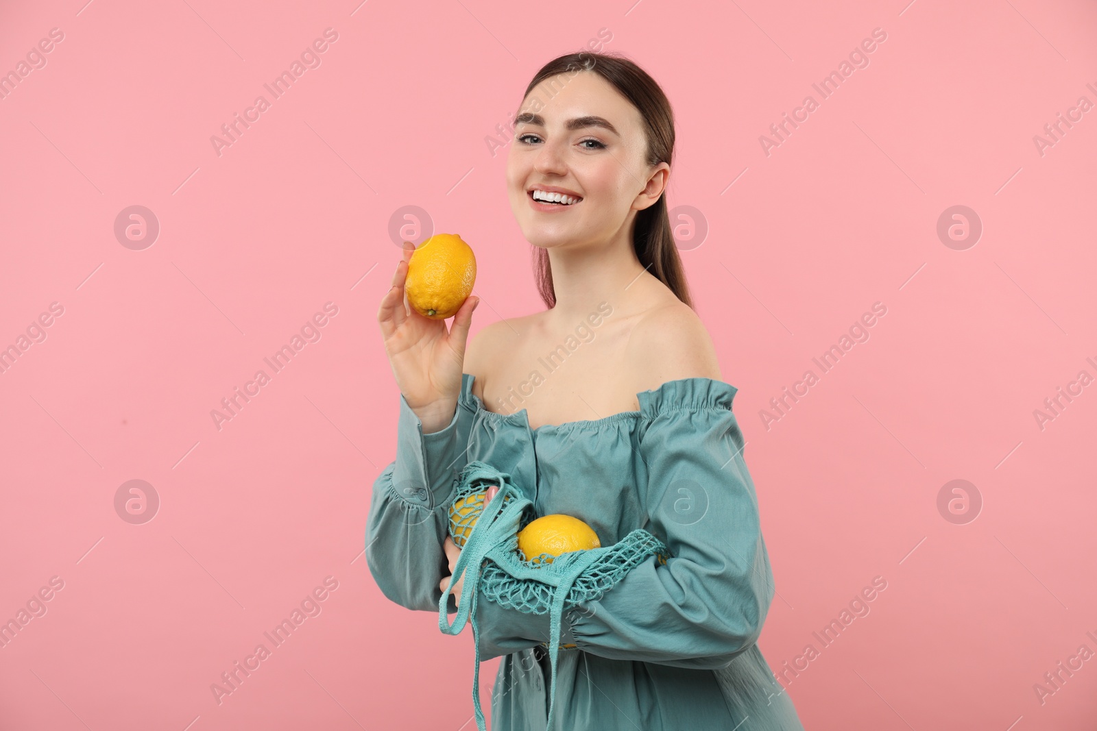 Photo of Woman with string bag of fresh lemons on pink background