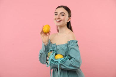 Woman with string bag of fresh lemons on pink background