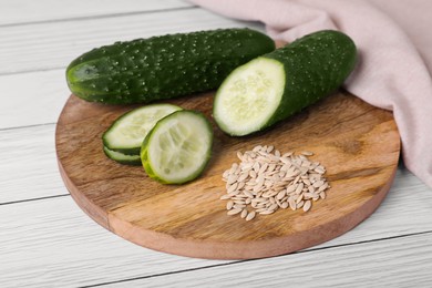 Pile of vegetable seeds and fresh cucumbers on white wooden table