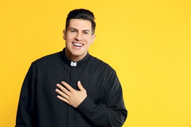 Photo of Priest in cassock with clerical collar laughing on yellow background. Space for text
