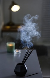 Photo of Incense sticks smoldering on table indoors, space for text