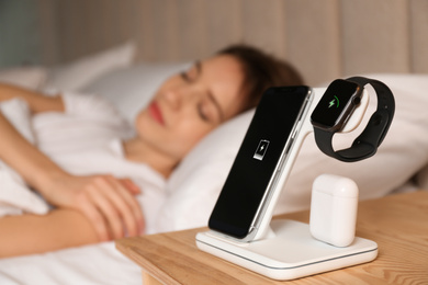 Photo of Smartphone, watch, earphones charging on wireless pad and sleeping woman in room