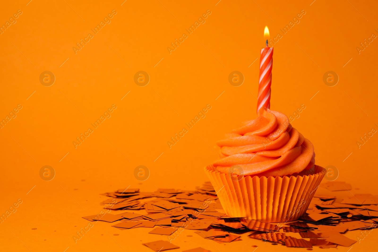 Photo of Delicious birthday cupcake with burning candle on orange background. Space for text