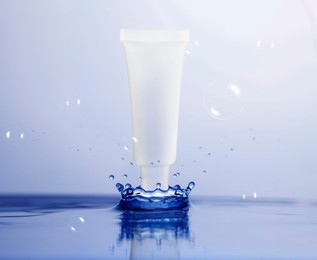 Image of Tube of cosmetic products and splashing water on light blue background. Space for design