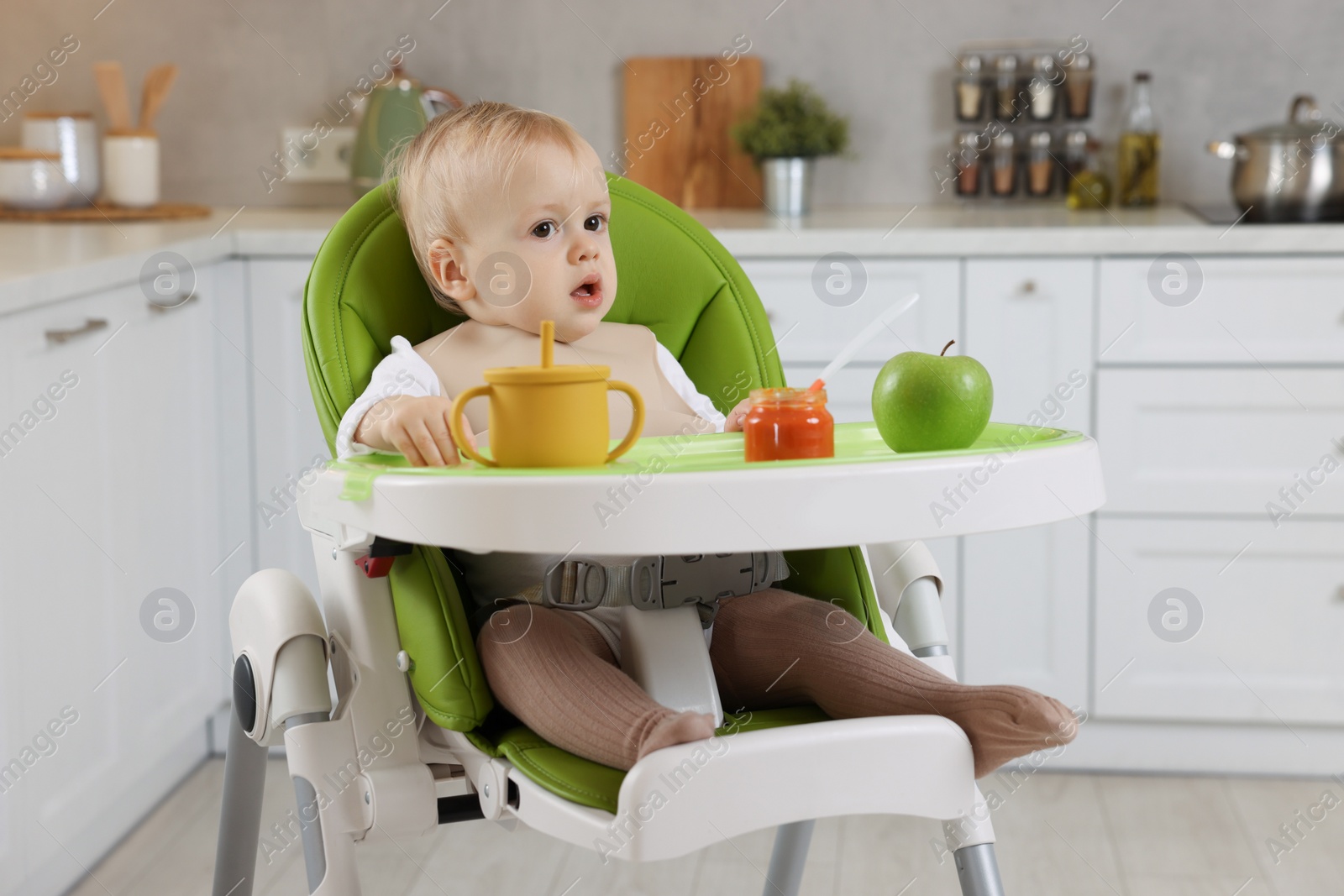Photo of Cute little baby with healthy food in high chair at home
