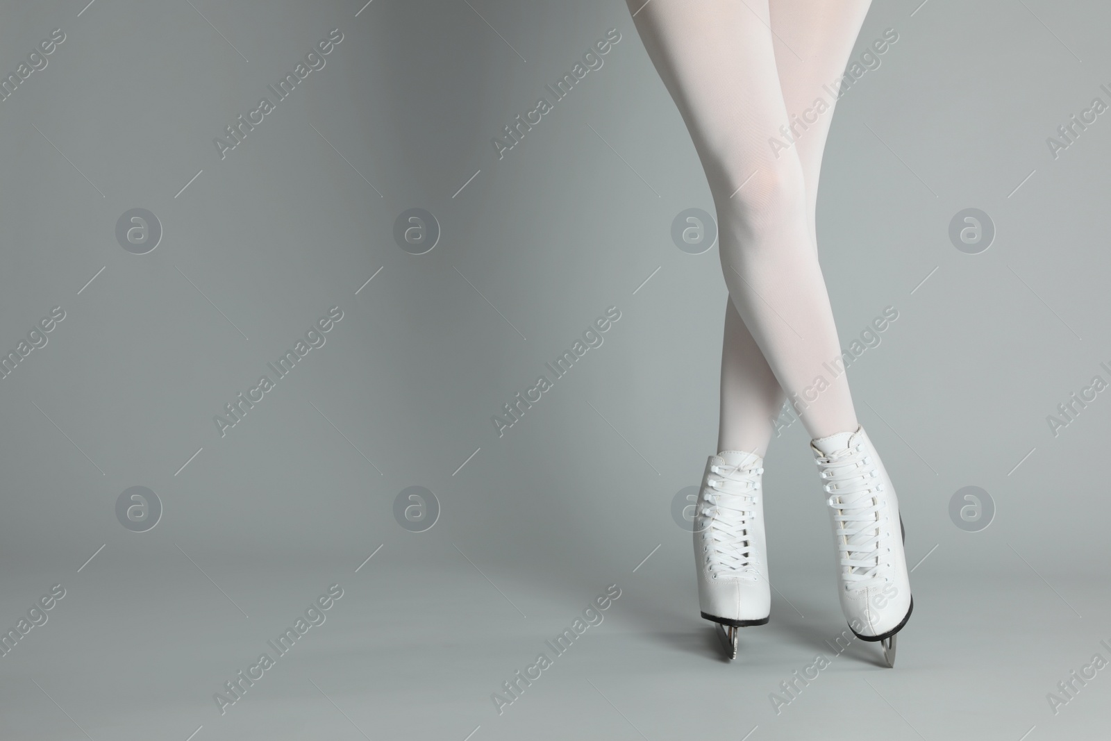 Photo of Woman in elegant white ice skates on grey background, closeup of legs. Space for text