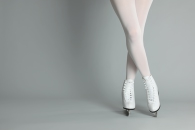 Woman in elegant white ice skates on grey background, closeup of legs. Space for text