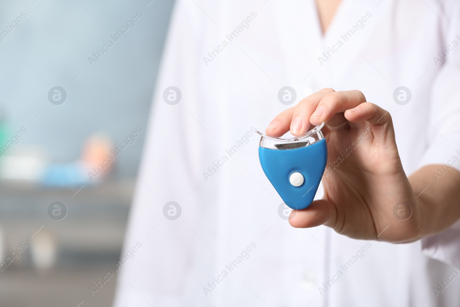 Photo of Female dentist holding teeth whitening device on blurred background, space for text