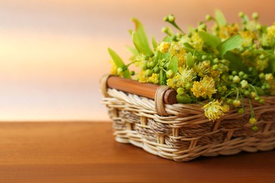 Photo of Beautiful linden blossoms and green leaves in wicker basket on wooden table. Space for text