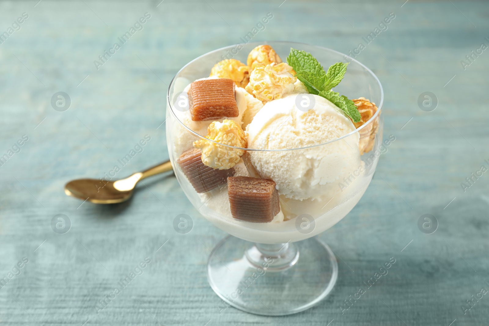 Photo of Delicious ice cream with caramel candies and popcorn in dessert bowl on blue wooden table