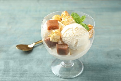 Photo of Delicious ice cream with caramel candies and popcorn in dessert bowl on blue wooden table