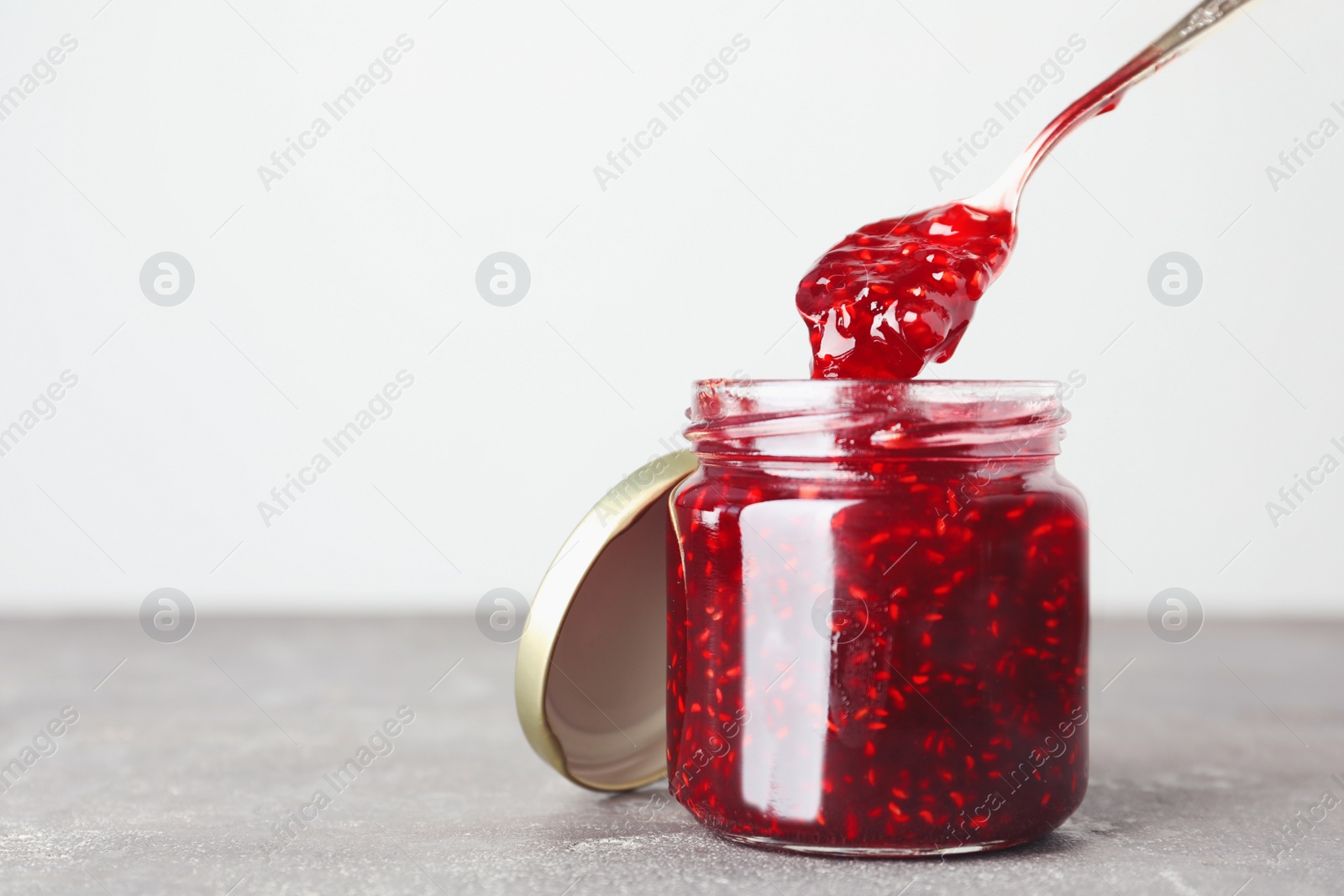 Photo of Sweet raspberry jam on grey table. Space for text