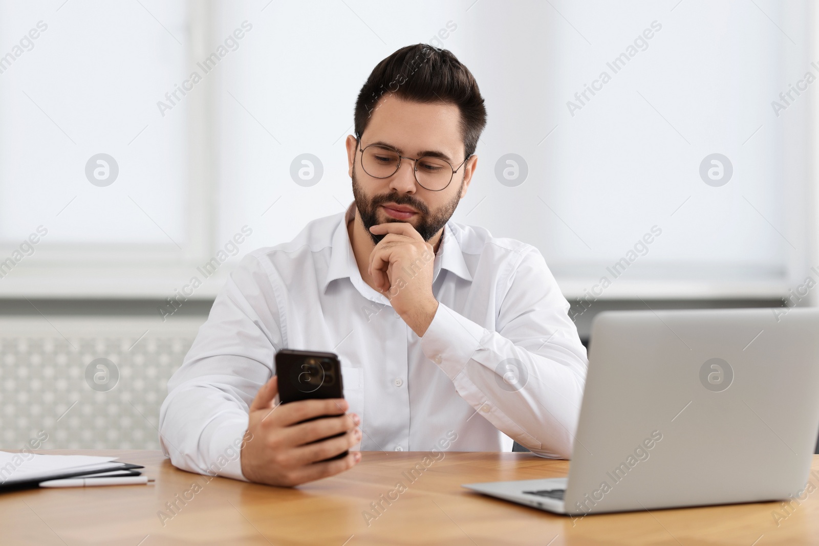 Photo of Young man using smartphone at wooden table in office