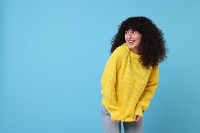 Photo of Happy young woman in stylish yellow sweater on light blue background, space for text