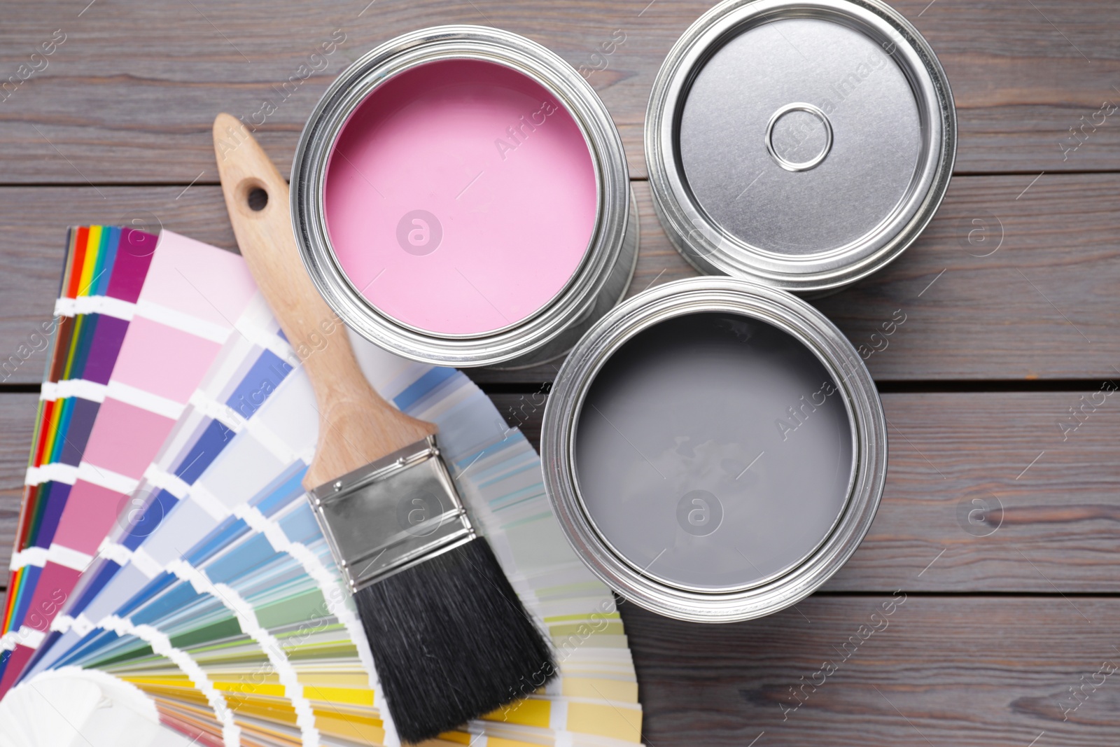 Photo of Cans of pink and grey paints, palette with brush on wooden table, flat lay
