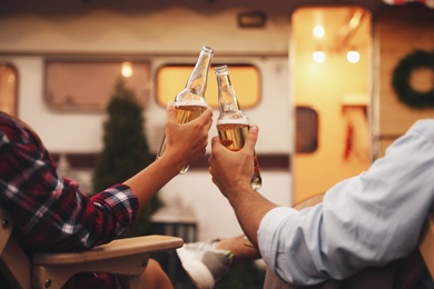 Photo of Young couple toasting with bottles of beer near trailer, closeup. Camping season