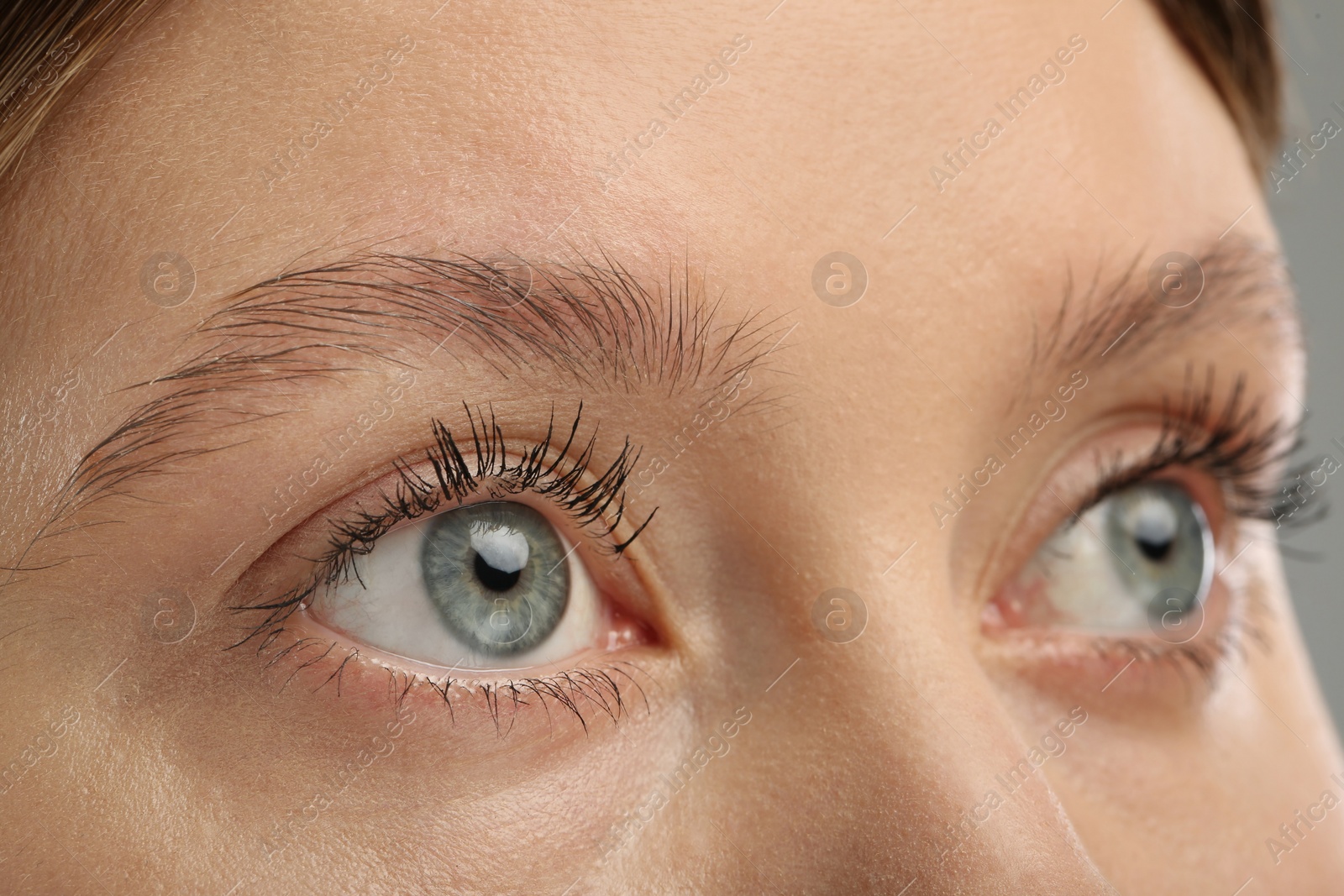 Photo of Woman with long eyelashes after mascara applying against grey background, closeup