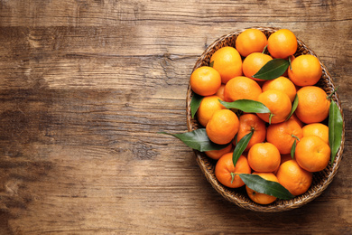 Photo of Fresh ripe tangerines with leaves and space for text on wooden table, top view. Citrus fruit