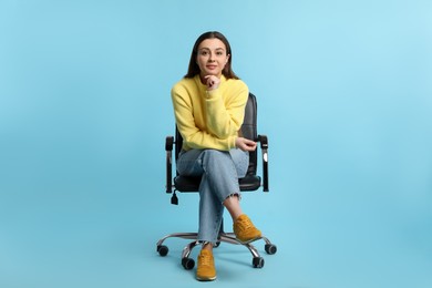 Young woman sitting in comfortable office chair on turquoise background