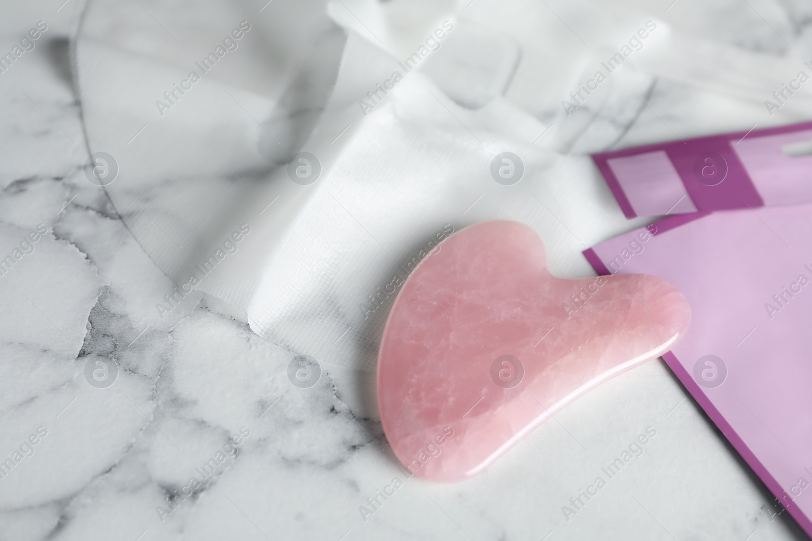 Photo of Rose quartz gua sha tool and facial mask on white marble table