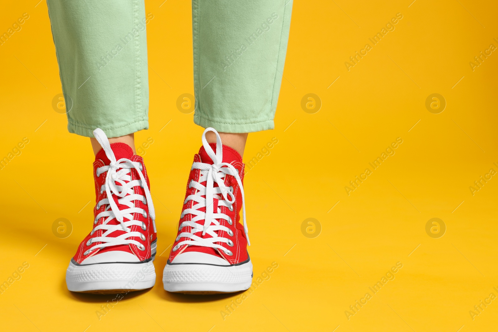 Photo of Woman in stylish gumshoes on yellow background, closeup. Space for text