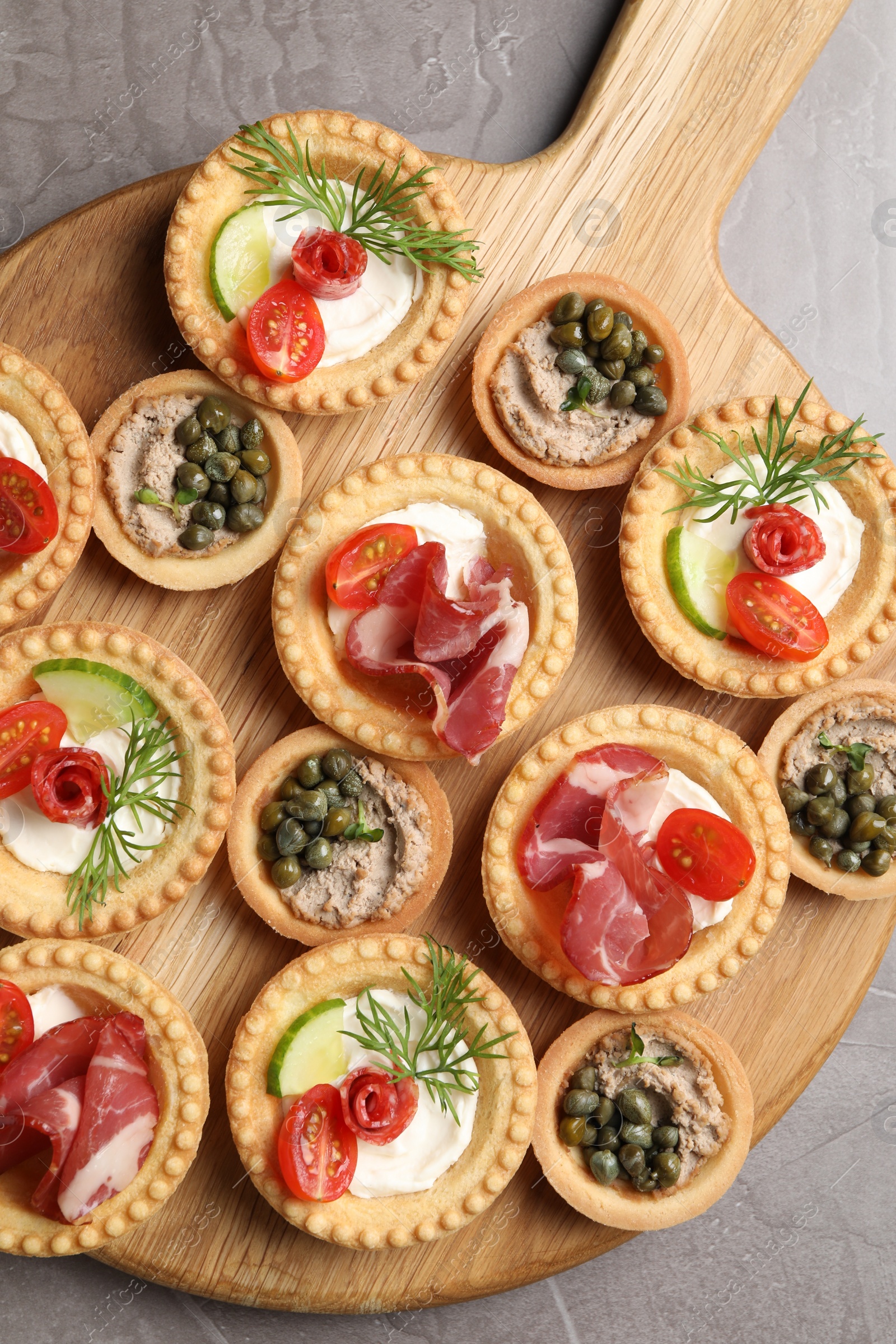 Photo of Delicious canapes with jamon, pate and dry smoked sausages on grey textured table, top view