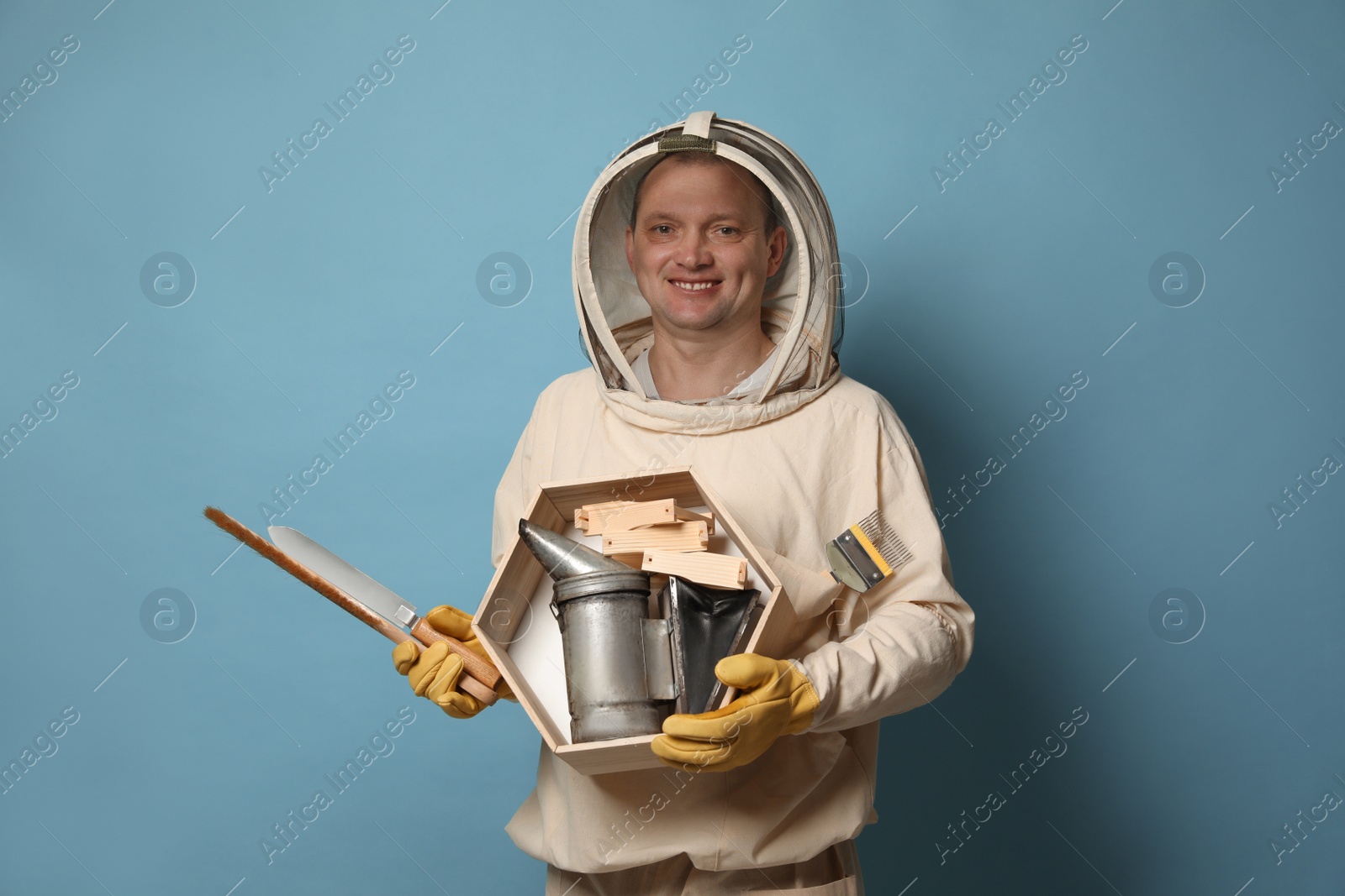 Photo of Beekeeper in uniform with tools on light blue background