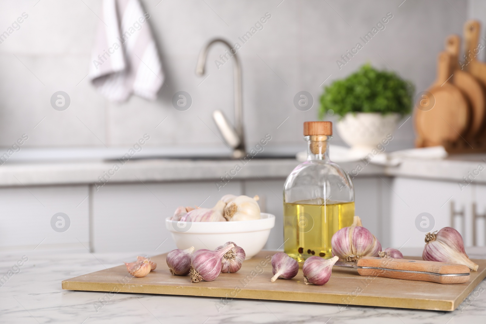 Photo of Fresh raw garlic, knife and oil on white marble table, space for text