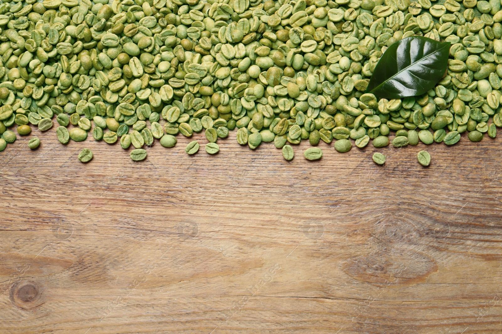 Photo of Many green coffee beans and leaf on wooden table, flat lay. Space for text