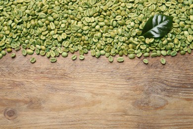 Many green coffee beans and leaf on wooden table, flat lay. Space for text