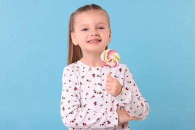 Happy little girl with colorful lollipop swirl on light blue background
