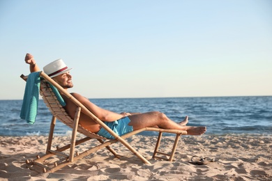 Young man relaxing in deck chair on beach near sea