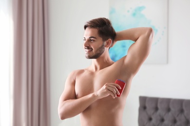 Photo of Handsome young man applying deodorant in room