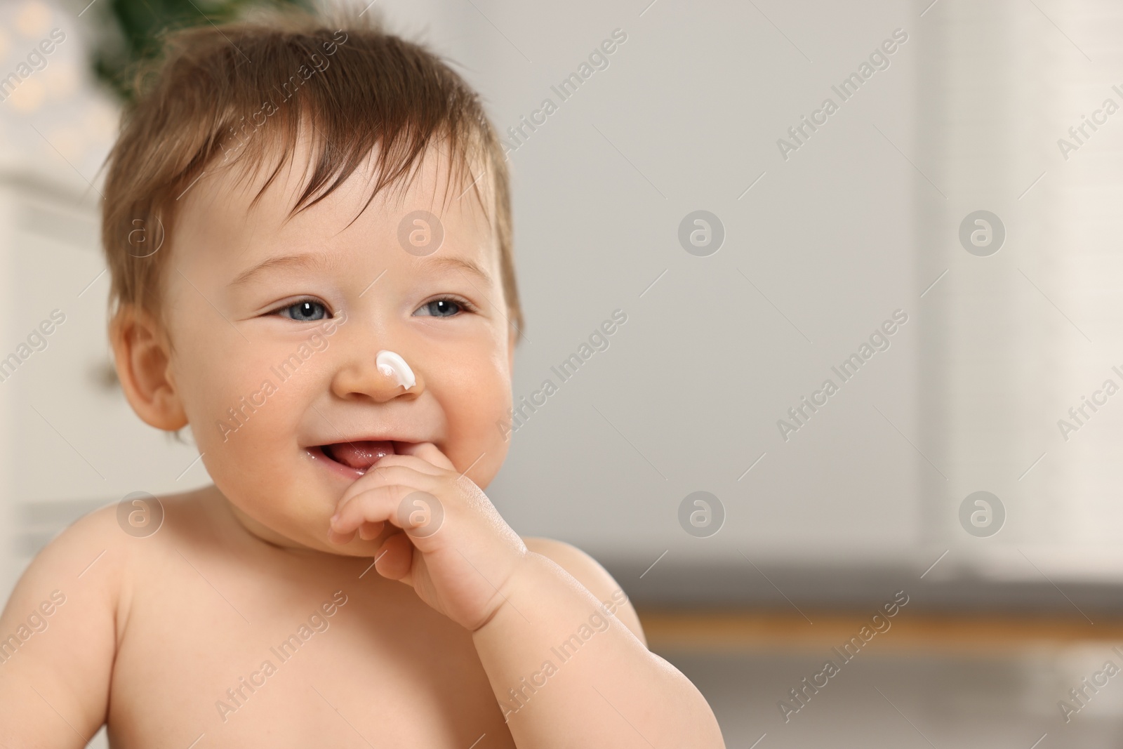 Photo of Cute little baby with moisturizing cream on face indoors, space for text