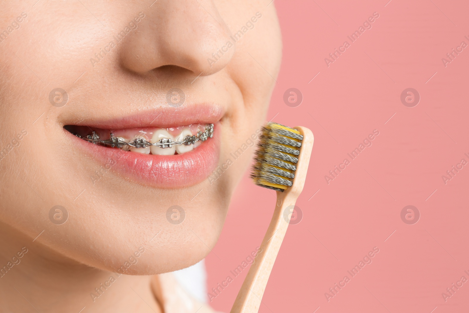 Photo of Smiling woman with dental braces and toothbrush on pink background, closeup. Space for text