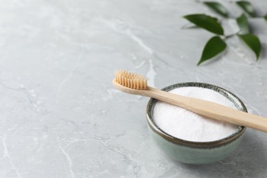 Bamboo toothbrush and bowl of baking soda on light gray marble table, space for text