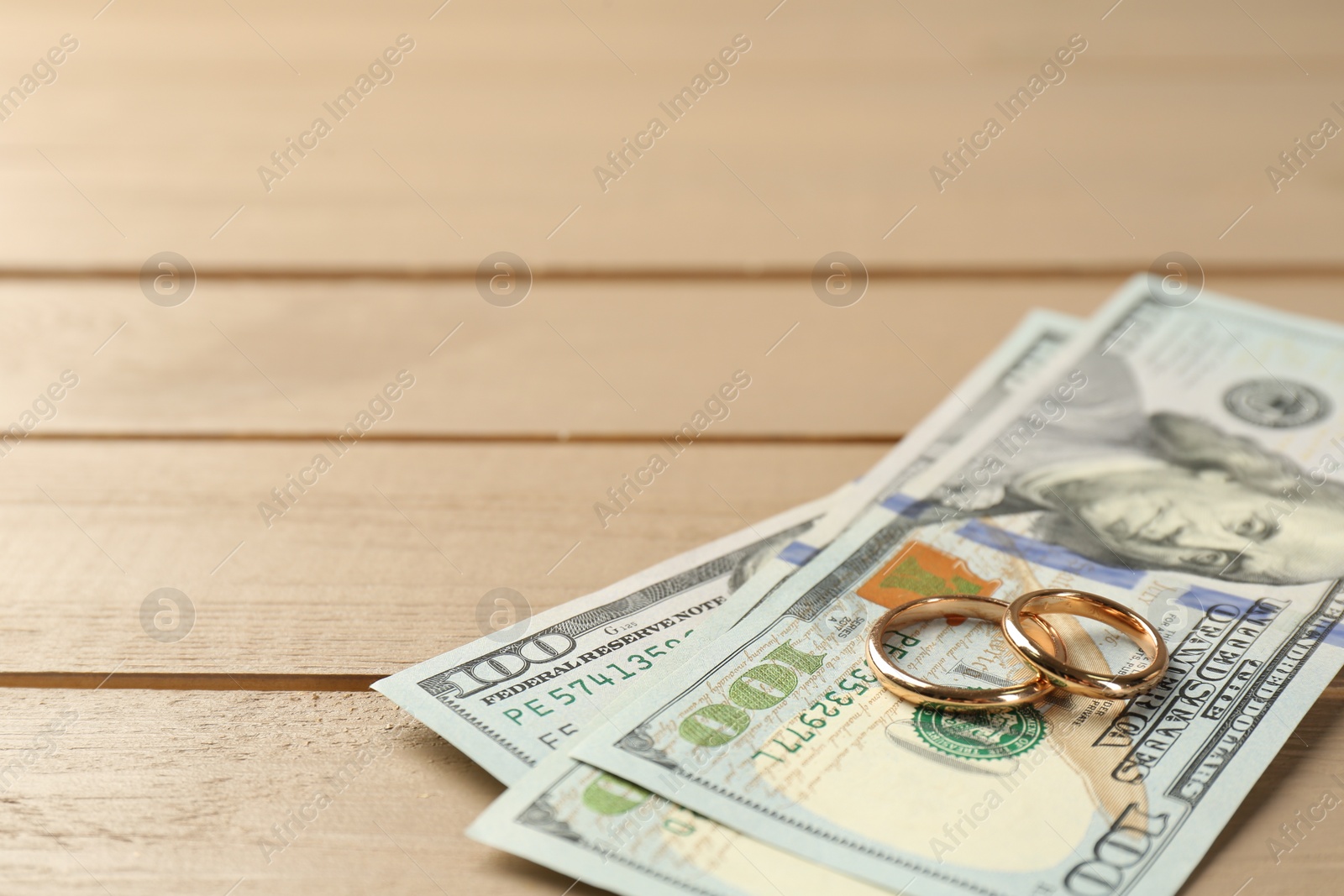 Photo of Honeymoon concept. Dollar banknotes and golden rings on wooden table, closeup. Space for text