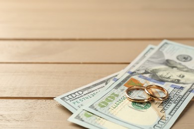 Honeymoon concept. Dollar banknotes and golden rings on wooden table, closeup. Space for text