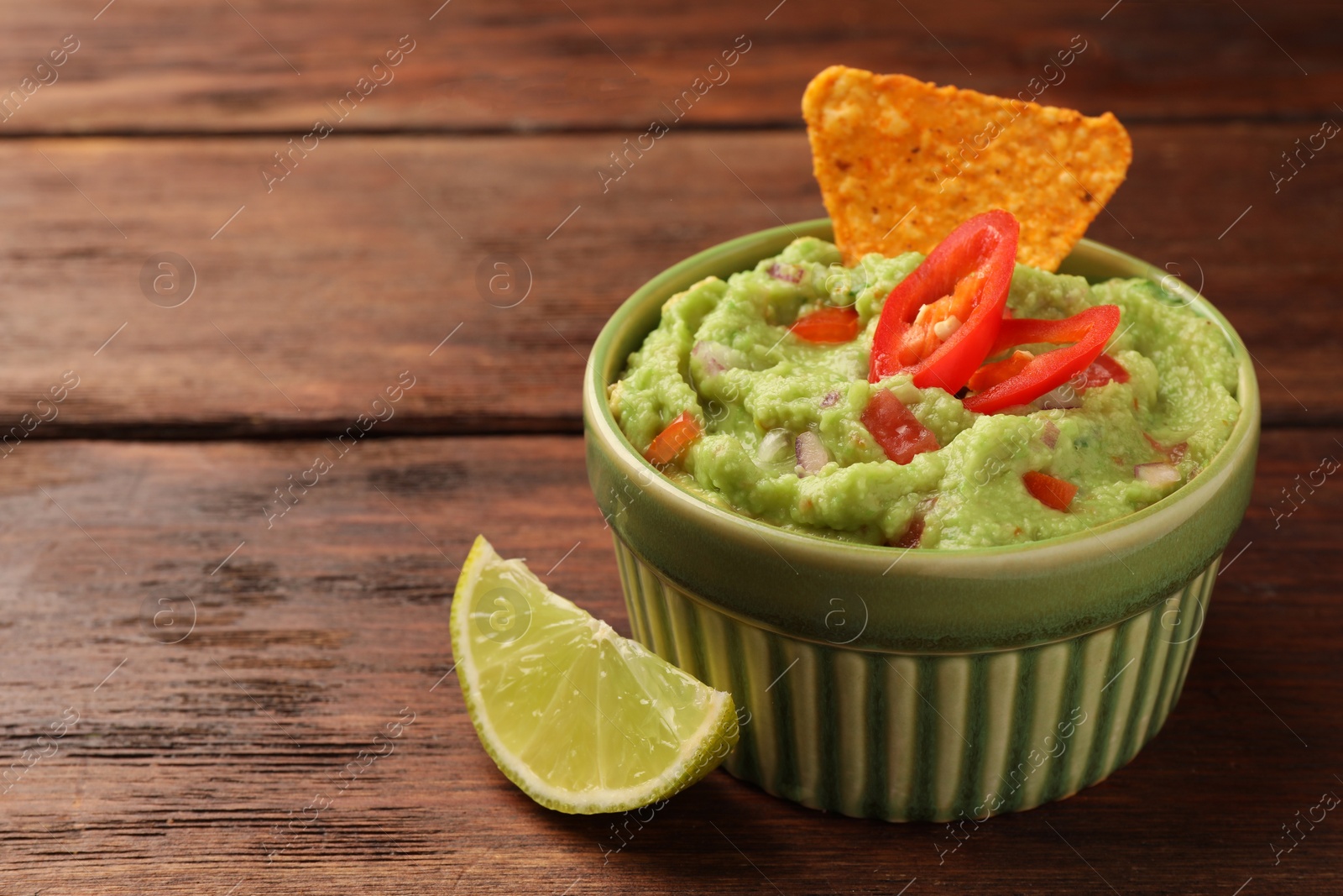 Photo of Bowl of delicious guacamole, nachos chips and lime on wooden table, closeup. Space for text