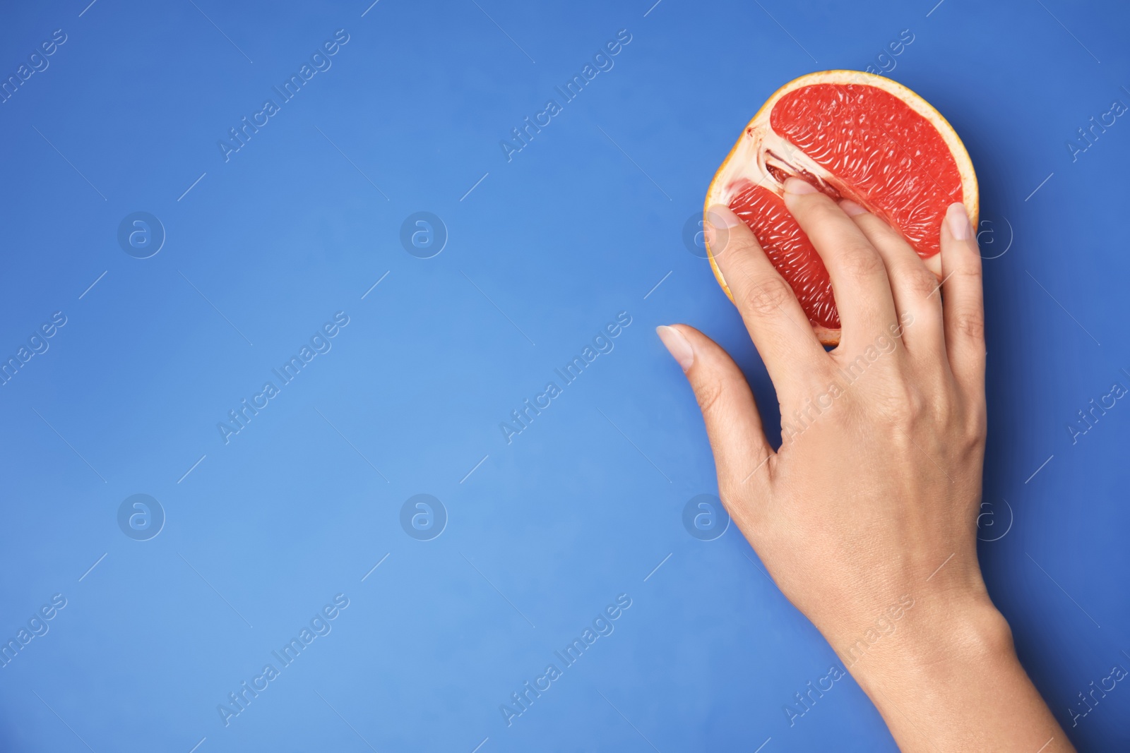 Photo of Young woman touching half of grapefruit on blue background, top view with space for text. Sex concept