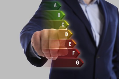 Energy efficiency. Man touching colorful rating on digital screen against light grey background, closeup