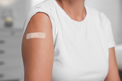 Photo of Woman with adhesive bandage on her arm after vaccination against blurred background, closeup