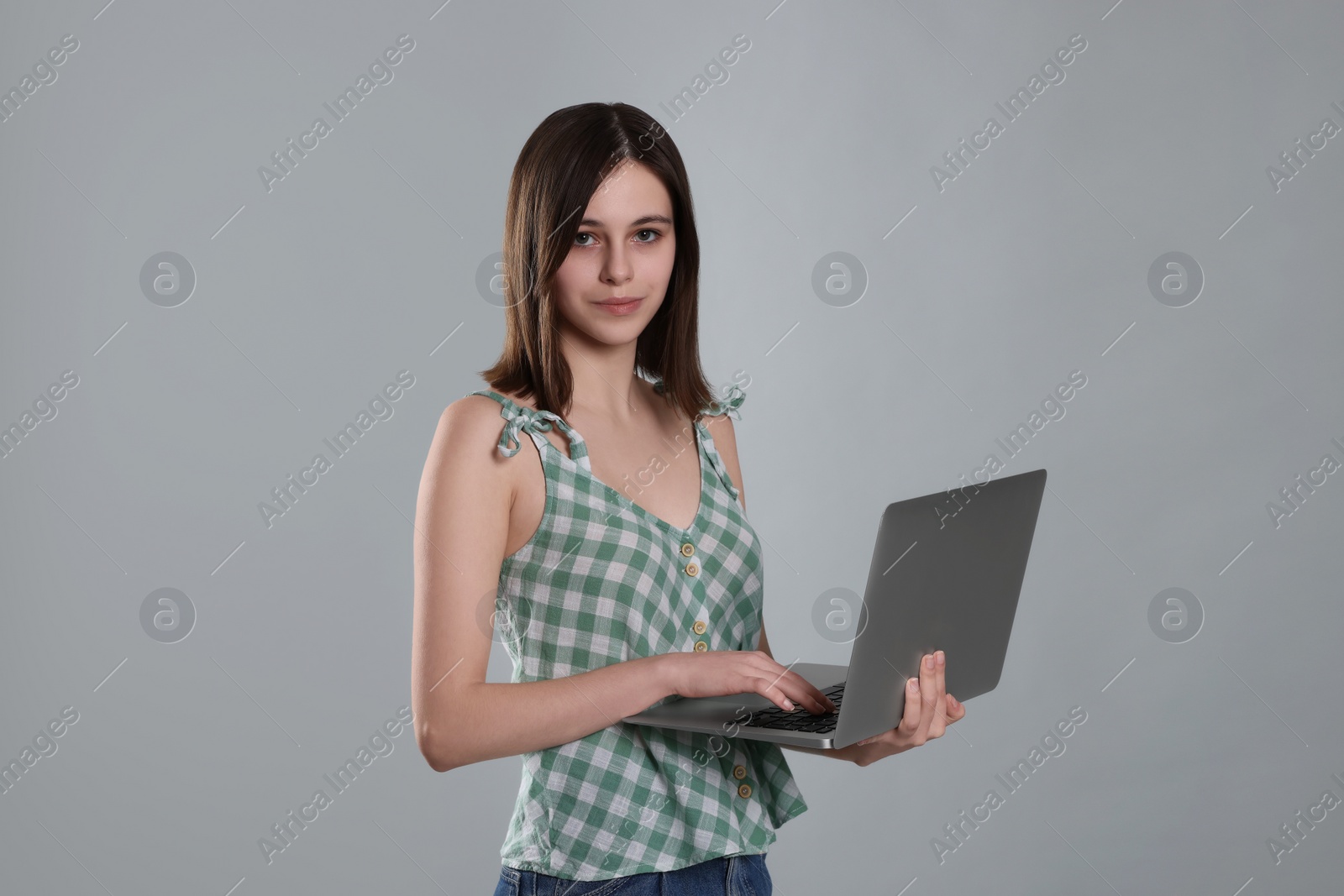 Photo of Cute teenage girl with laptop on light grey background
