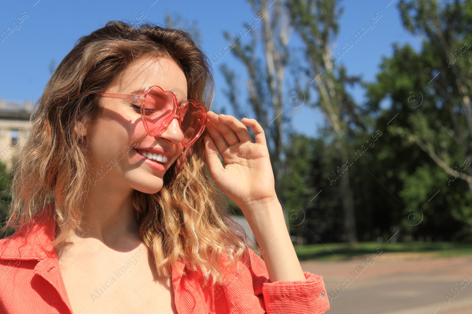 Photo of Portrait of happy woman with heart shaped glasses in city on sunny day. Space for text