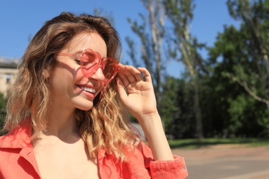 Photo of Portrait of happy woman with heart shaped glasses in city on sunny day. Space for text