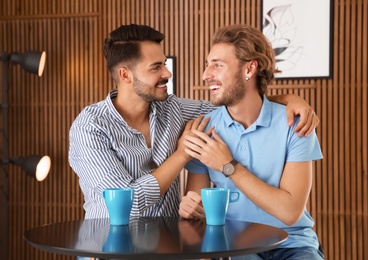 Happy gay couple with coffee at table indoors
